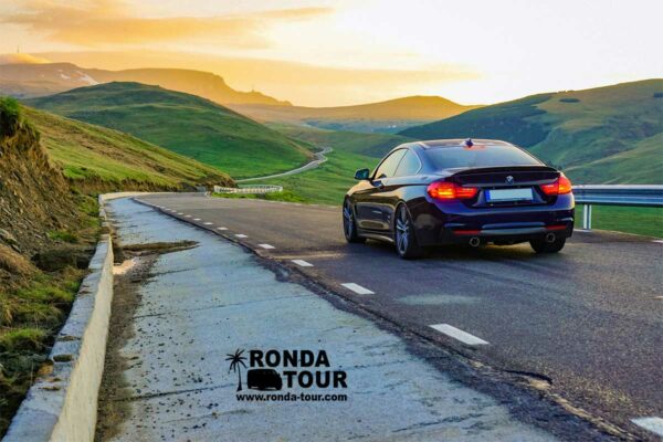 BMW sur l'asphalte dans un environnement vallonné. Filigrane avec le logo de Ronda Tour et son adresse web www.ronda-tour.com sur la photo.