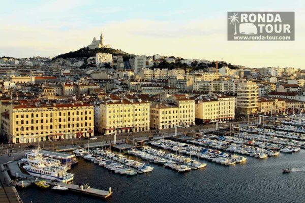 Vieux Port de Marseille et Basilique Notre Dame de la Garde sous le soleil. Filigrane avec le logo de Ronda Tour et son adresse web www.ronda-tour.com sur la photo.