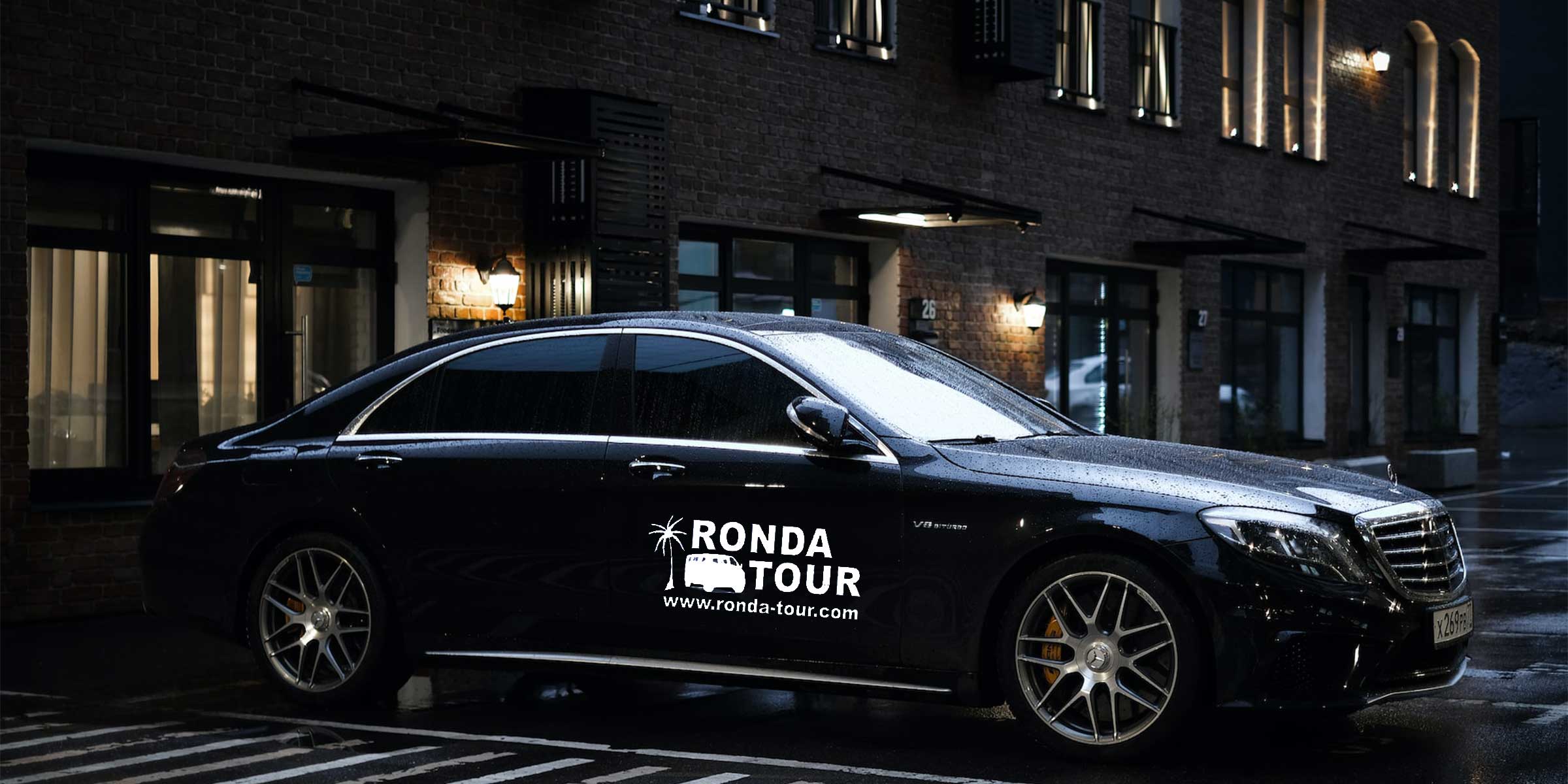 Photo d'une Mercedes S-Class garée devant un immeuble, de nuit, avec le logo de Ronda Tour et son adresse web www.ronda-tour.com