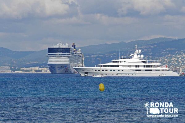 Un bateau de Croisière et un Yacht côte à côte dans la baie de Cannes. Filigrane avec le logo de Ronda Tour et son adresse web www.ronda-tour.com sur la photo.